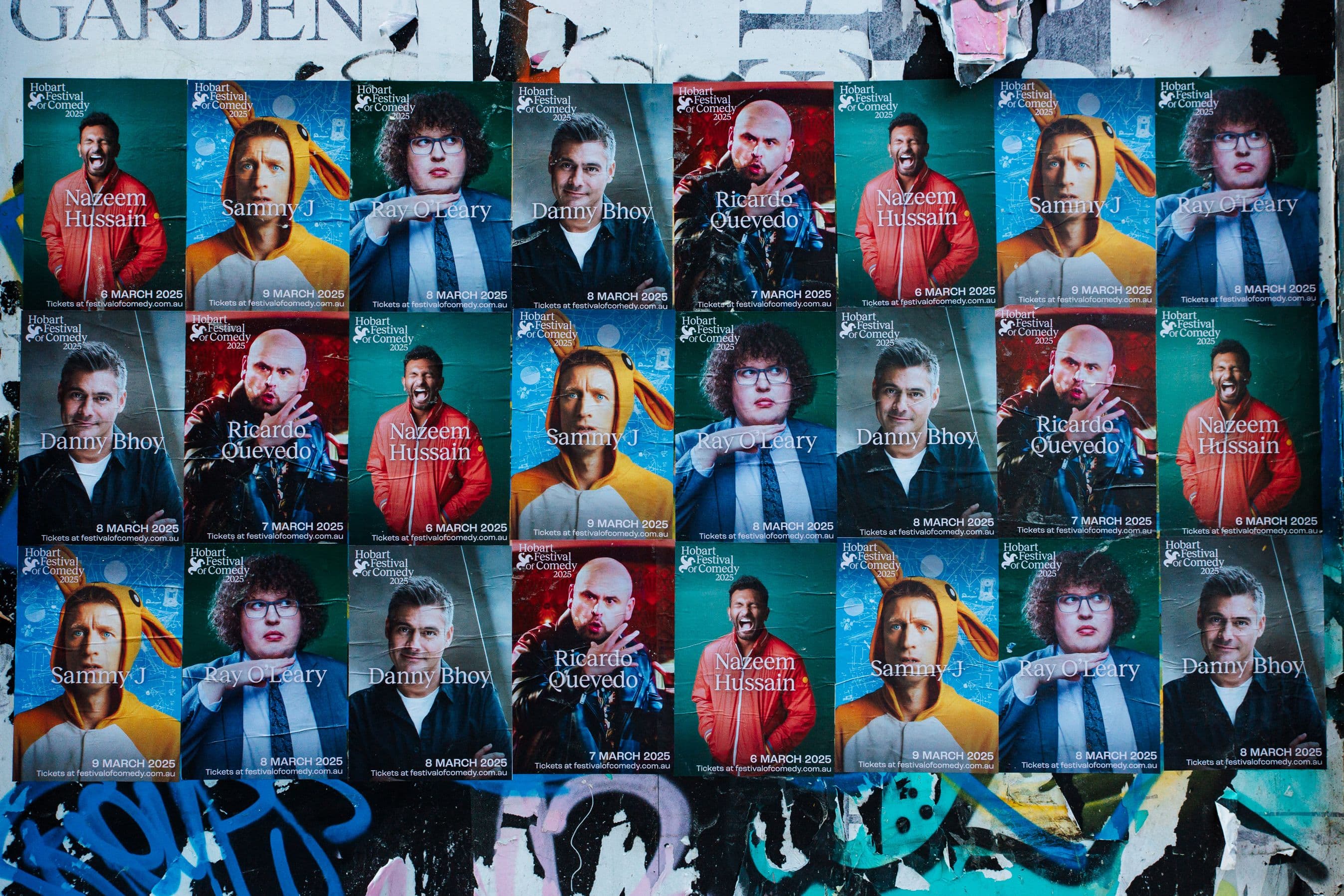 An array of Hobart Festival of Comedy posters are pasted on a wall.