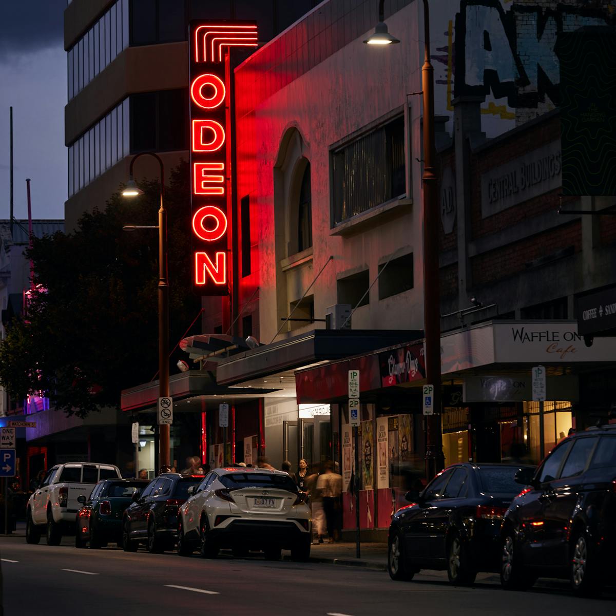 A view of cars in the street with a neon sign in the background that reads Odeon